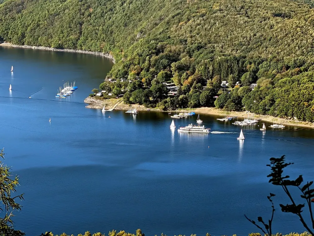 Blick vom Aussichtspunkt Hirschley auf den tiefblauen Rurstausee mit Segelbooten und bewaldeten Uferhängen