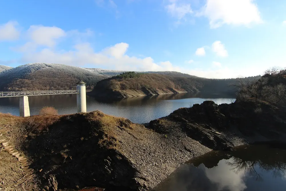 Blick von der Urftstaumauer über den Urftsee, links Brücke und Turm, dahinter bewaldete Höhenzüge