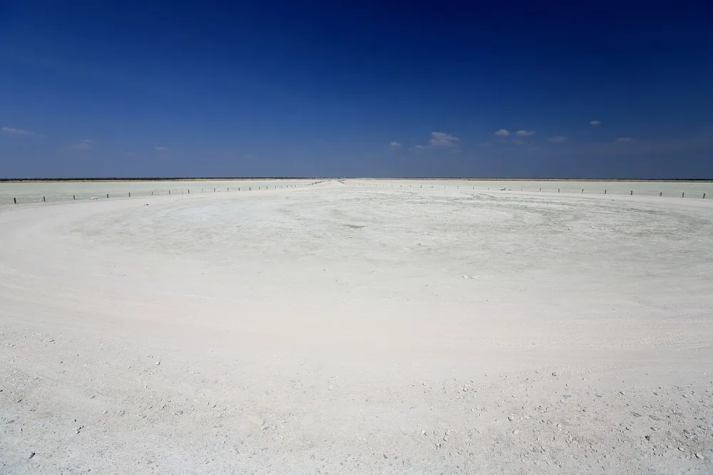Etosha Lookout: gleißend weiße, völlig flache Salzpfanne bis zum Horizont unter tiefblauem Himmel