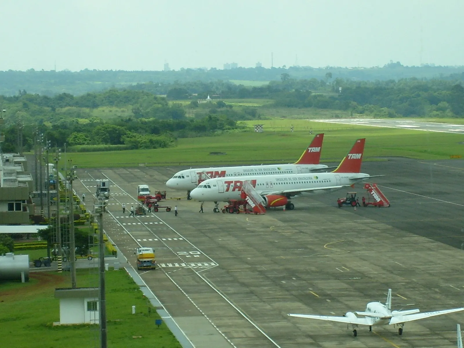 Vorfeld des Flughafens Foz do Iguaçu von oben mit zwei Verkehrsflugzeugen der TAM und einem Kleinflugzeug, dahinter grüne Hügel