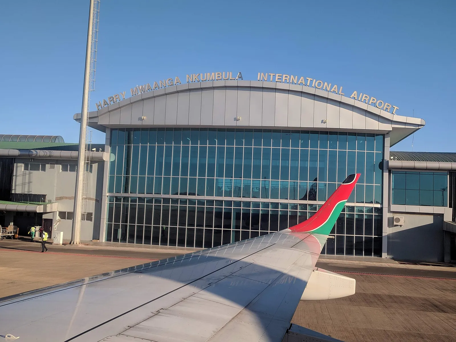 Terminal des Harry Mwaanga Nkumbula International Airport in Livingstone mit Glasfront und Schriftzug, vorn die Tragfläche eines Flugzeugs