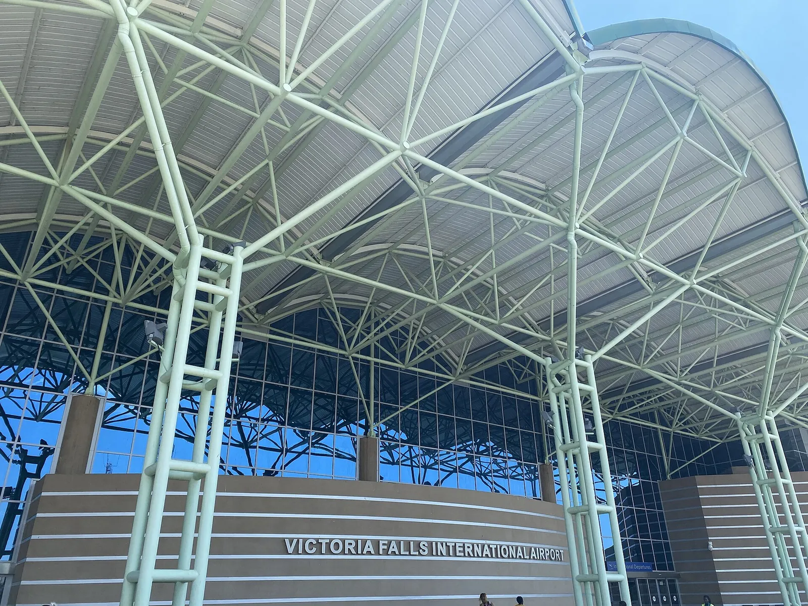 Stahlrohr-Dach am Eingang des Victoria Falls International Airport mit dem Schriftzug am Terminal
