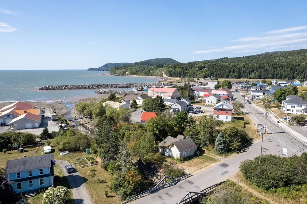 Luftaufnahme von Alma am Bay of Fundy: Häuser entlang der Hauptstraße, Hafenmole und bewaldete Küste
