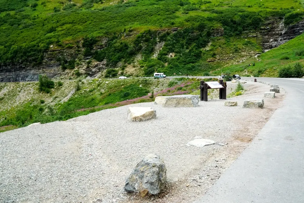 Big Bend an der Going-to-the-Sun Road: Haltebucht mit Steinblöcken und Infotafeln unter grünen Berghängen