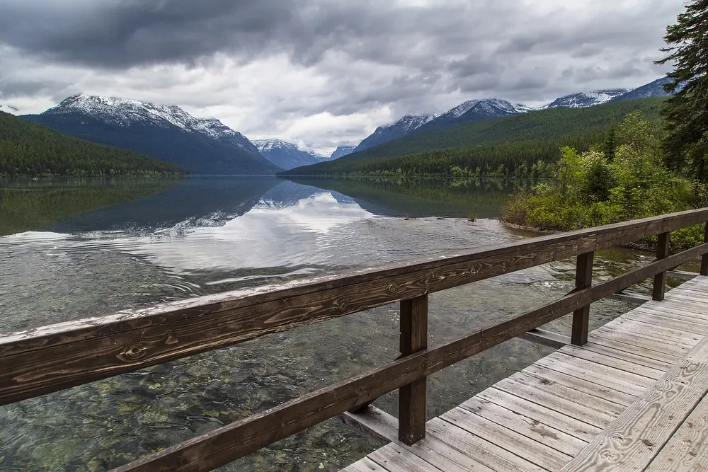 Holzsteg am Fuß des Bowman Lake, dahinter der langgestreckte See zwischen bewaldeten Bergen mit Spiegelungen