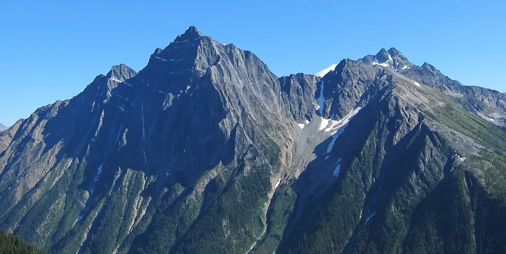 Mount Macdonald in den Selkirk Mountains: steiler, dunkler Felsgipfel mit Schneerinnen unter blauem Himmel