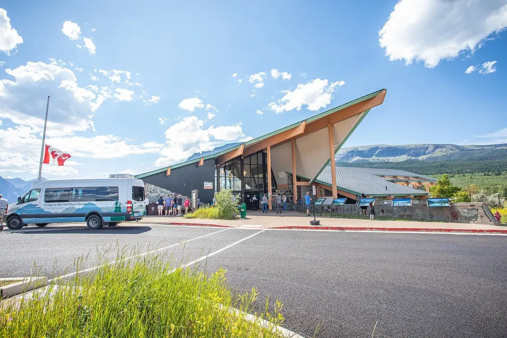 St. Mary Visitor Center: flacher Bau mit spitz aufragendem Dach, davor Vorplatz und ein Shuttlebus