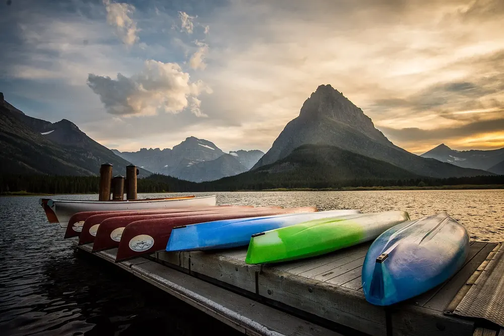 Kajaks und Kanus auf einem Steg am Swiftcurrent Lake, dahinter der spitze Grinnell Point im Abendlicht