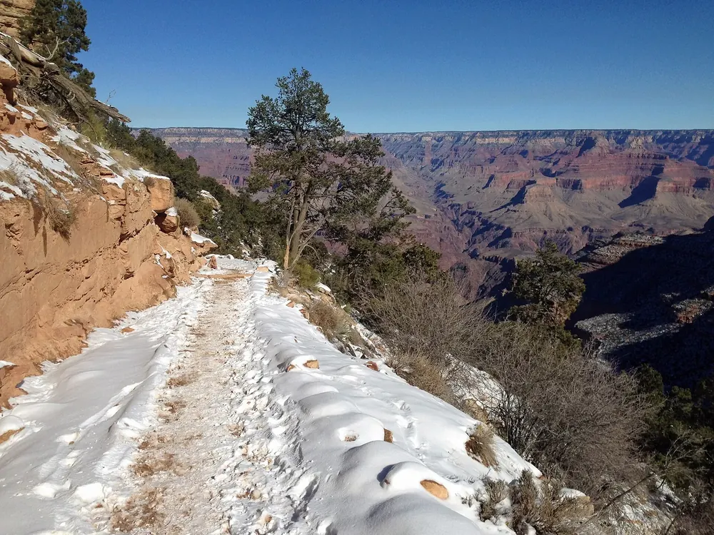 Verschneiter oberer Abschnitt des Bright Angel Trail am Canyonrand, dahinter die Weite des Grand Canyon