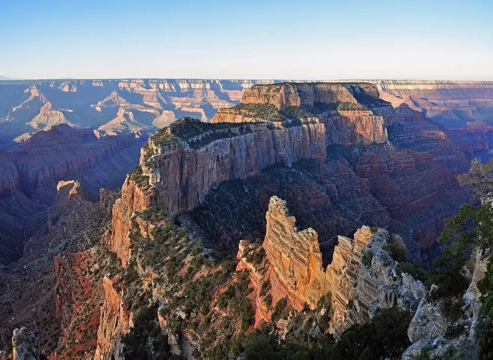 Sonnenaufgang am Cape Royal: rötlich leuchtende Felstürme und Tafelberge über dem weiten Grand Canyon