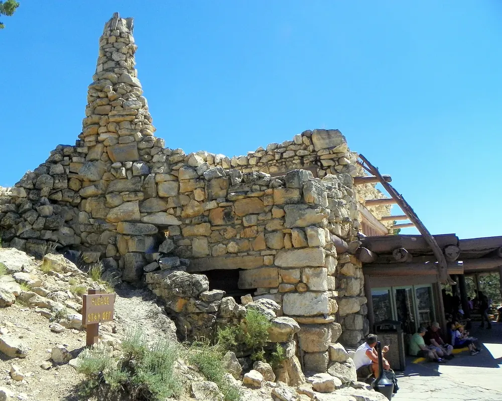Hermits Rest: rustikales Rasthaus aus Natursteinmauern mit hohem Kamin am Canyonrand, davor Felsen und Sträucher