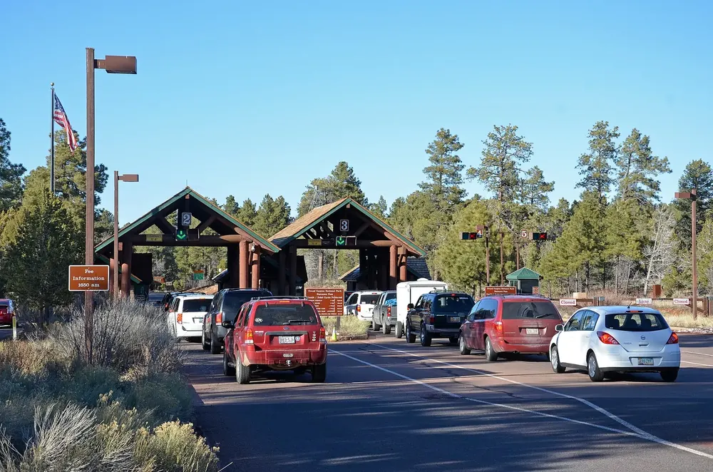 South Entrance Station des Grand Canyon: Kassenhäuschen unter Holzdächern, davor wartende Autos zwischen Kiefern