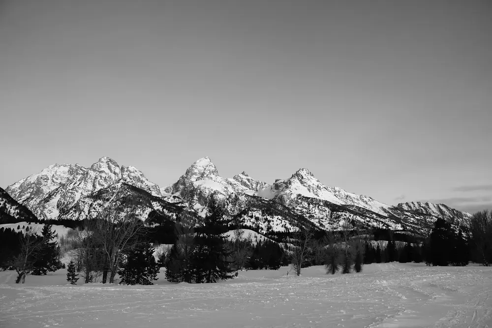 Verschneite Ebene am Taggart Lake Trailhead im Winter, dahinter die schneebedeckten Gipfel der Teton Range