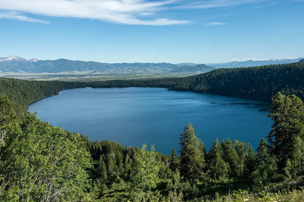 Blick vom Phelps Lake Overlook auf den tiefblauen Phelps Lake zwischen bewaldeten Hängen, dahinter die Ebene