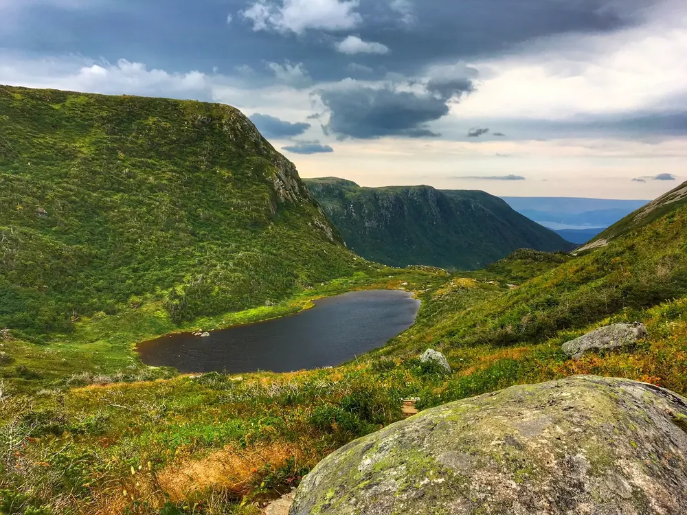 Beim Aufstieg zum Gros Morne: grünes Hochtal mit kleinem See zwischen steilen Hängen, hinten der Fjord