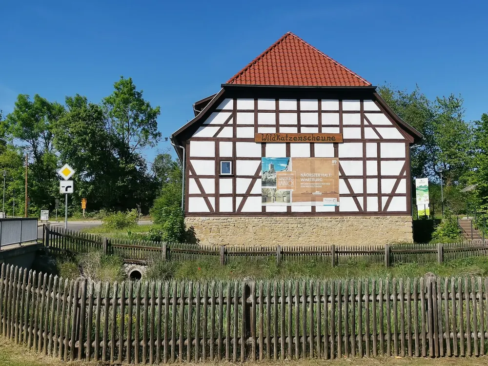 Fachwerkhaus mit rotem Ziegeldach im Wildkatzendorf Hütscheroda, davor ein Holzlattenzaun und Bäume