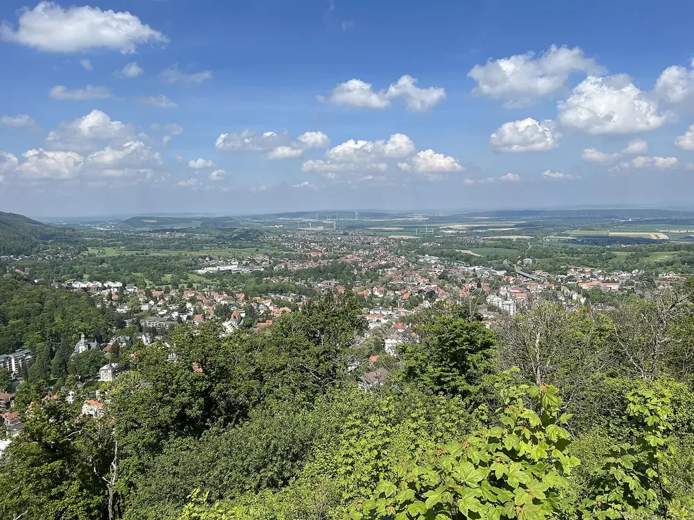 Aussicht vom Großen Burgberg auf Bad Harzburg: Häuser zwischen viel Grün, dahinter weites Harzvorland unter Wolken