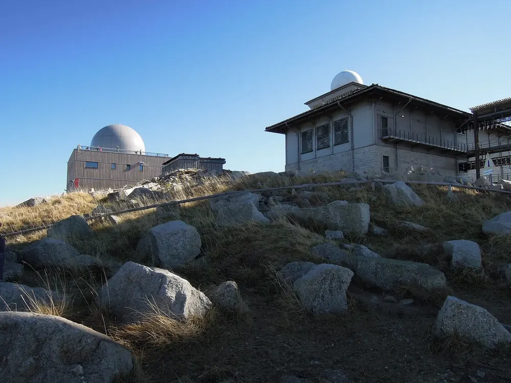 Brockenhaus mit weißer Kuppel und die Brockenherberge auf dem Gipfel, davor Granitblöcke im Morgenlicht