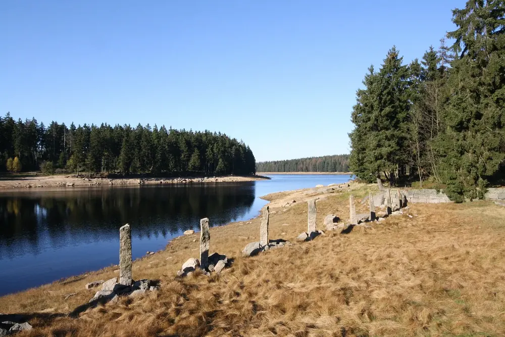Oderteich nahe dem Parkplatz: steinerne Obelisken vor dem Überlauf, dahinter der Stausee und Fichtenwald