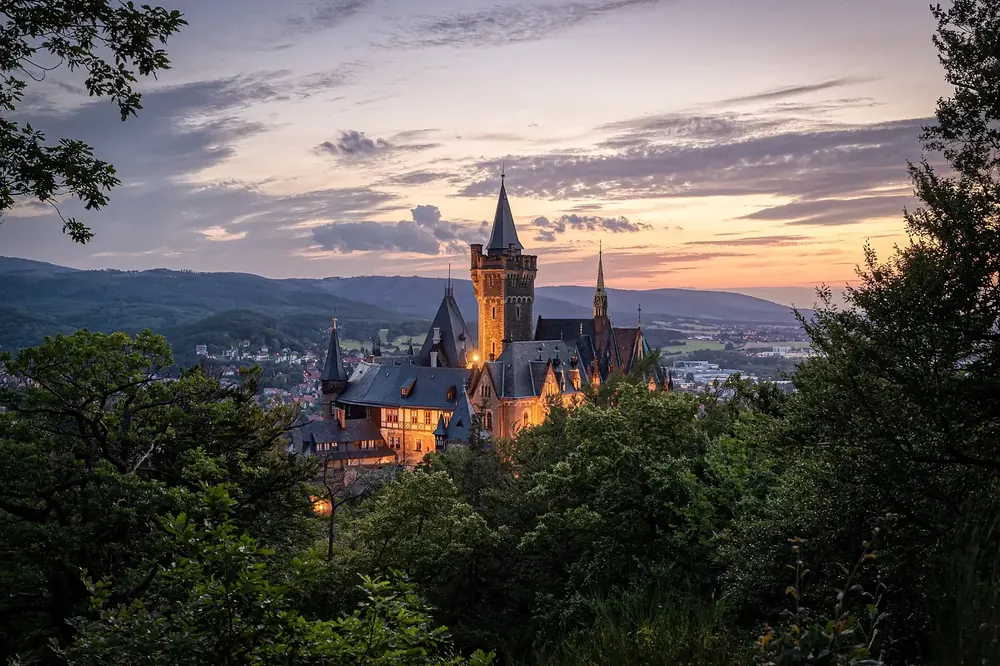 Schloss Wernigerode nach Sonnenuntergang: beleuchtetes Schloss mit Türmen über der Stadt und bewaldeten Hügeln