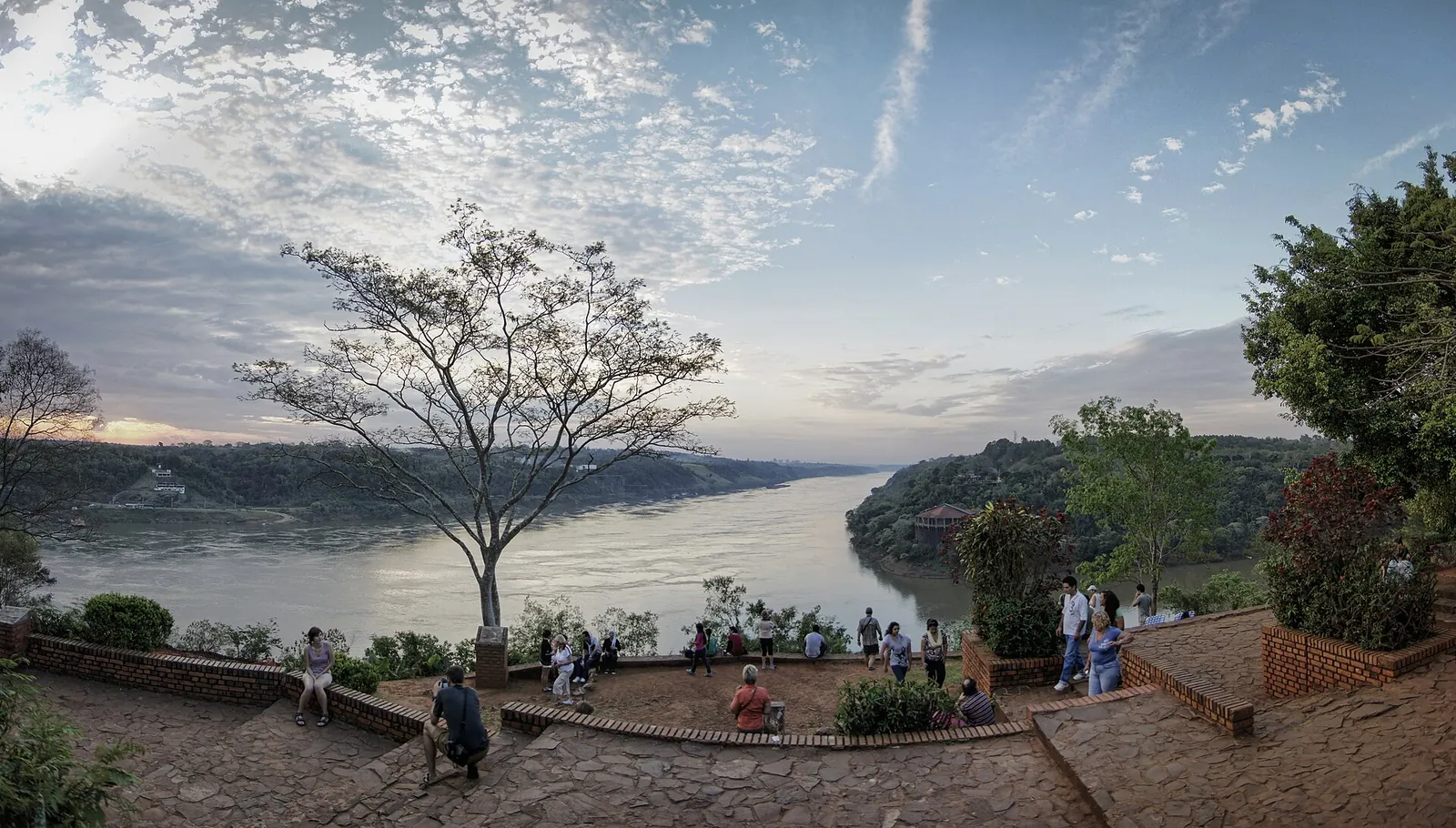 Aussichtsplatz am Hito Tres Fronteras in Puerto Iguazú mit Blick auf den Zusammenfluss von Iguazú und Paraná, ein einzelner Baum vor bewölktem Himmel