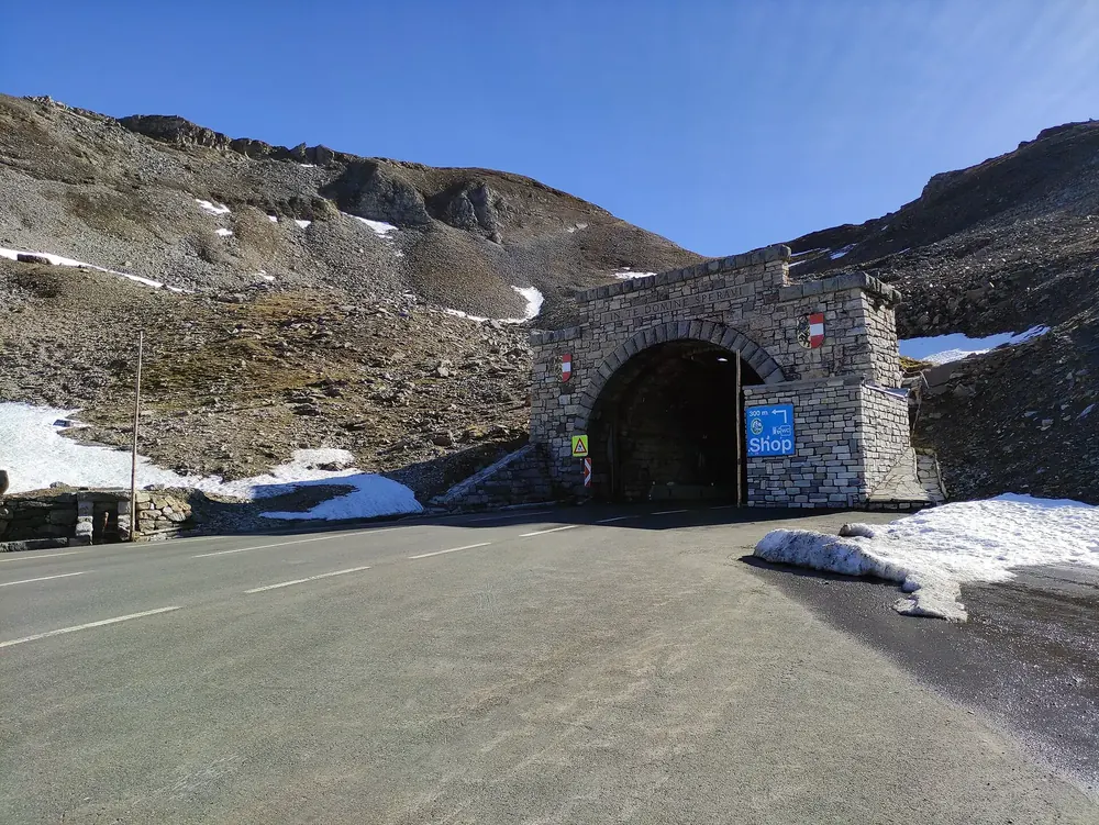 Nordportal des Hochtortunnels an der Großglockner-Hochalpenstraße: gemauerter Tunnelbogen zwischen Schneeresten und Geröll