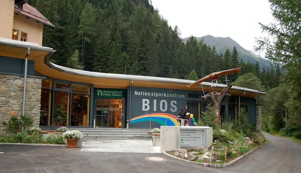 Nationalparkzentrum BIOS in Mallnitz: Eingangsbau mit geschwungenem Dach und Schriftzug, dahinter Bergwald