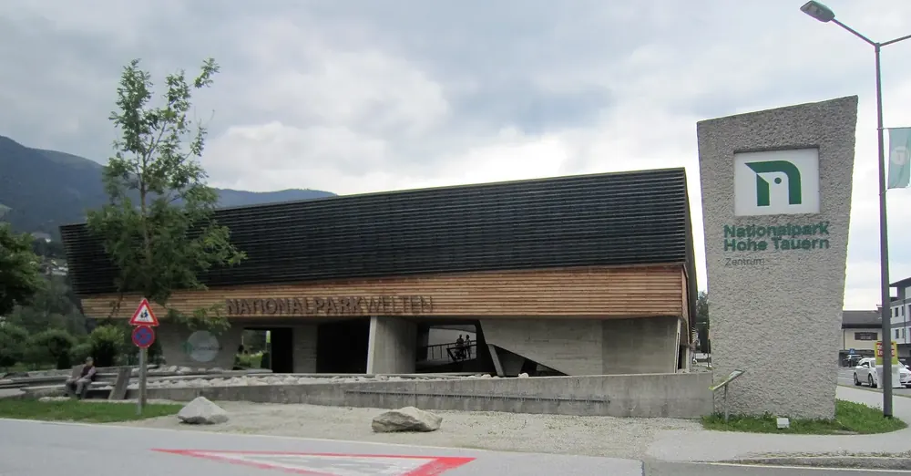 Nationalparkwelten in Mittersill: flaches Besucherzentrum mit Holzfassade, davor Pylon mit Nationalpark-Logo