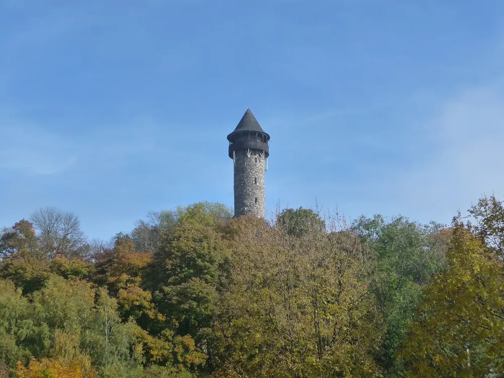 Der Turm der Burg Wildenburg bei Kempfeld ragt über herbstlich gefärbte Bäume in den blauen Himmel