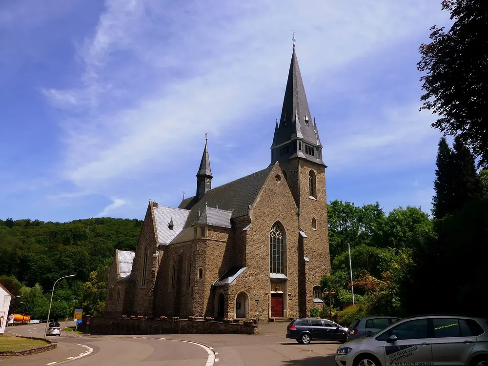 Katholische Kirche St. Hubertus in Nonnweiler: Bruchsteinkirche mit spitzem Turm an einer Straßenkreuzung