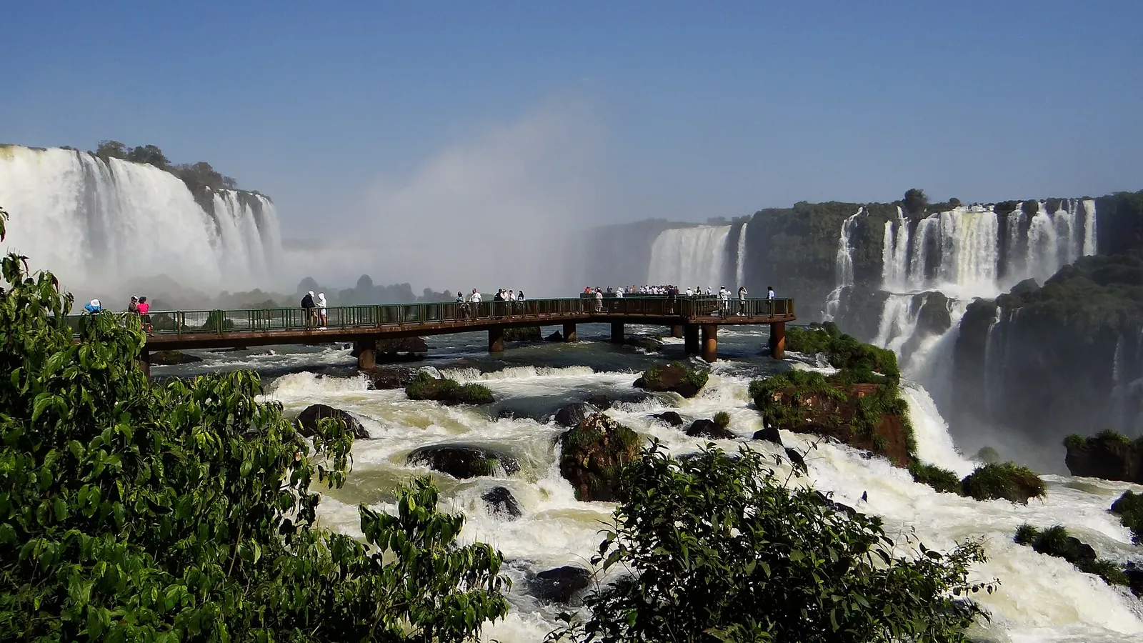 Der Aussichtssteg zur Garganta do Diabo im Iguaçu-Nationalpark führt über Stromschnellen auf die Fälle zu, links und rechts hohe Fallstufen in der Gischt