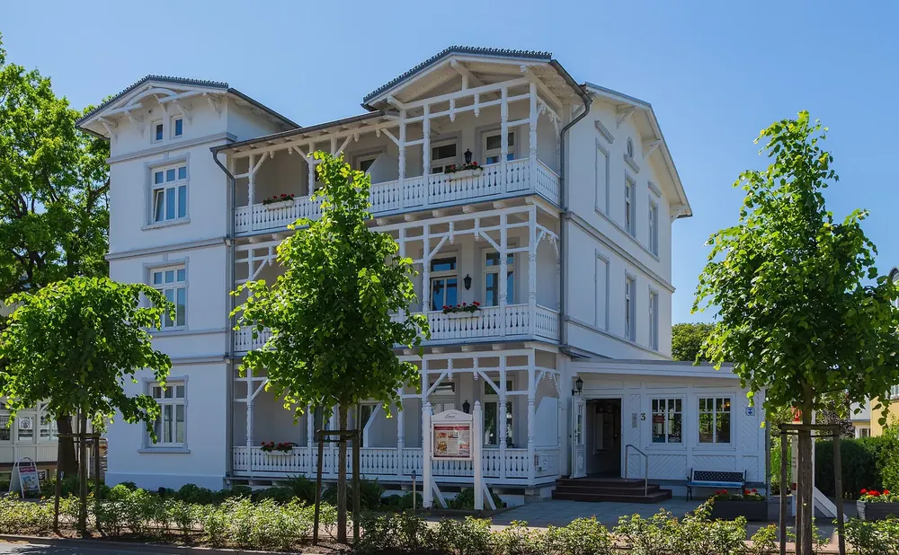Hotel Getreuer Eckart in Binz: weiße Bäderarchitektur mit Holzbalkonen und Veranden unter blauem Himmel