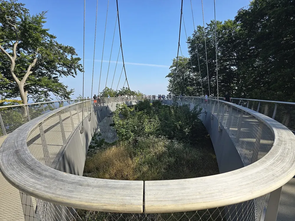 Skywalk Königsstuhl: ringförmiger Steg über den Baumkronen an Seilen, dahinter die Ostsee und Buchenwald