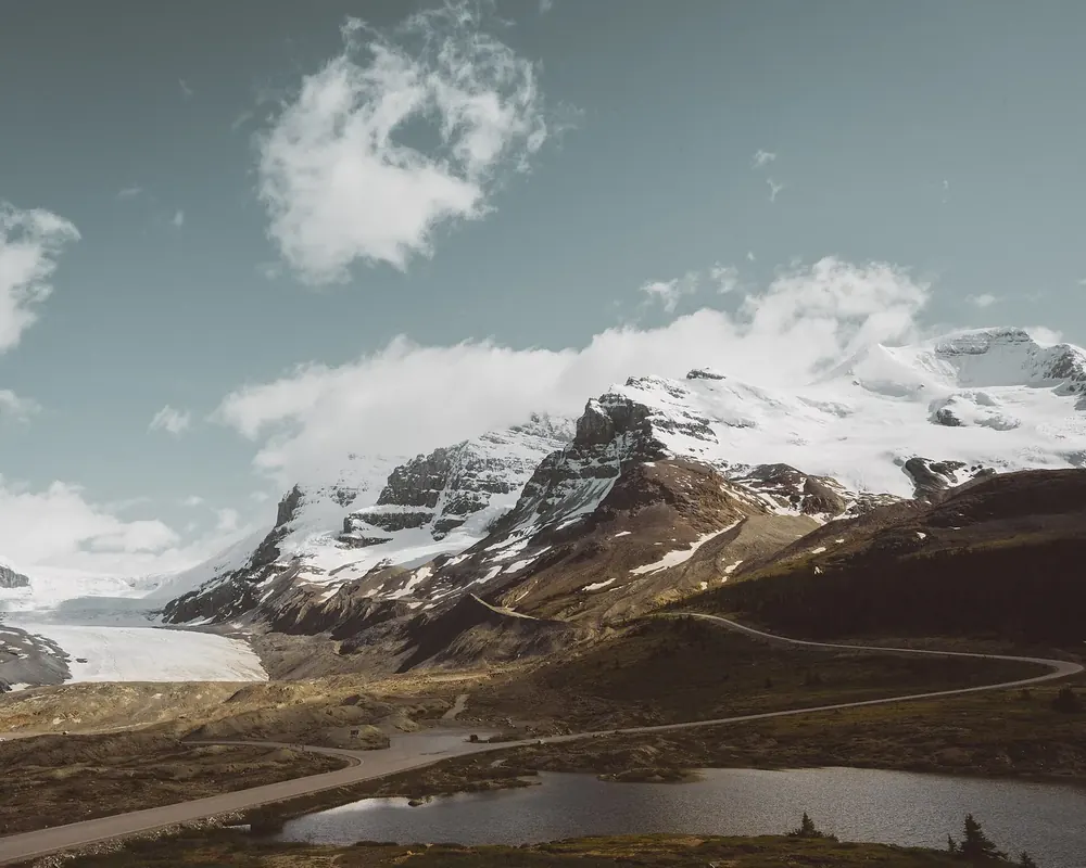 Athabasca-Gletscher: Gletscherzunge zwischen verschneiten Bergen, davor karges Moränengelände mit Straße und Tümpel