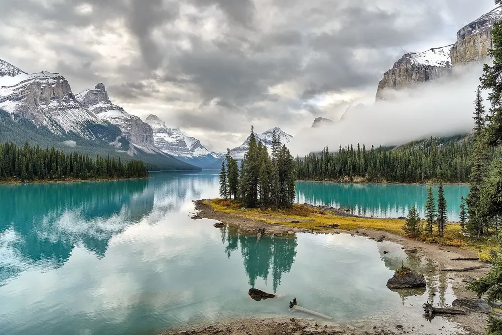 Spirit Island im Maligne Lake am Morgen: kleine Insel mit Fichten im türkisfarbenen Wasser vor Wolken und Gipfeln