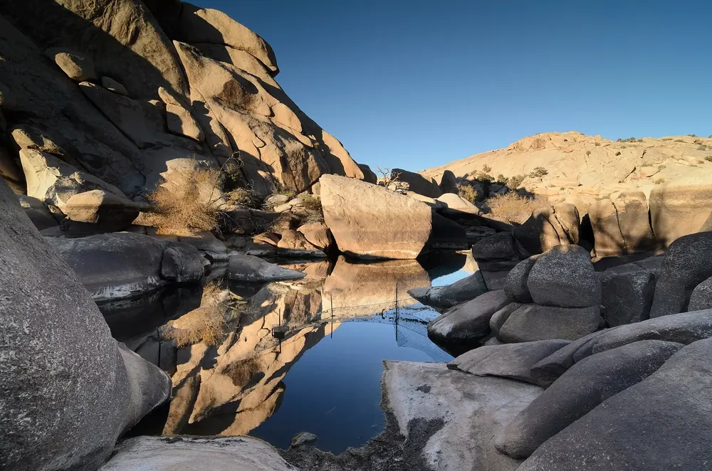 Barker Dam: aufgestautes Wasserbecken zwischen runden Granitfelsen, in dem sich die Felsen im Abendlicht spiegeln