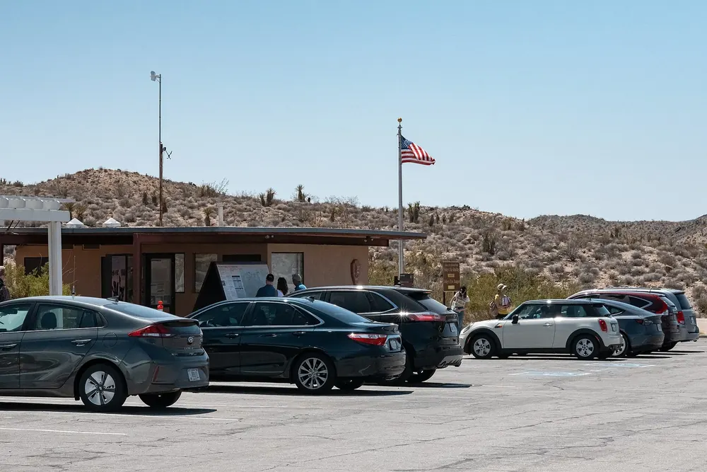 Cottonwood Visitor Center: flache hellbraune Gebäude mit Fahnenmast vor Wüstenhügeln, davor ein voller Parkplatz