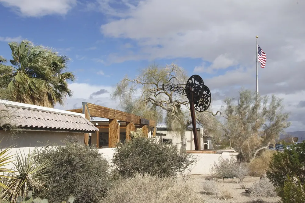 Oasis Visitor Center in Twentynine Palms: flache Gebäude mit Fahnenmast zwischen Fächerpalmen und Wüstenpflanzen