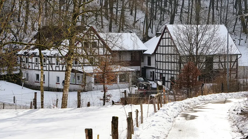 Siegmannsmühle bei Vöhl im Winter: weiße Fachwerkhäuser mit verschneiten Dächern am Waldrand