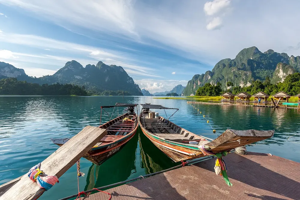 Cheow-Lan-Stausee des Rajjaprabha-Damms: Longtail-Boote am Steg, dahinter Kalksteinberge und Floßhütten