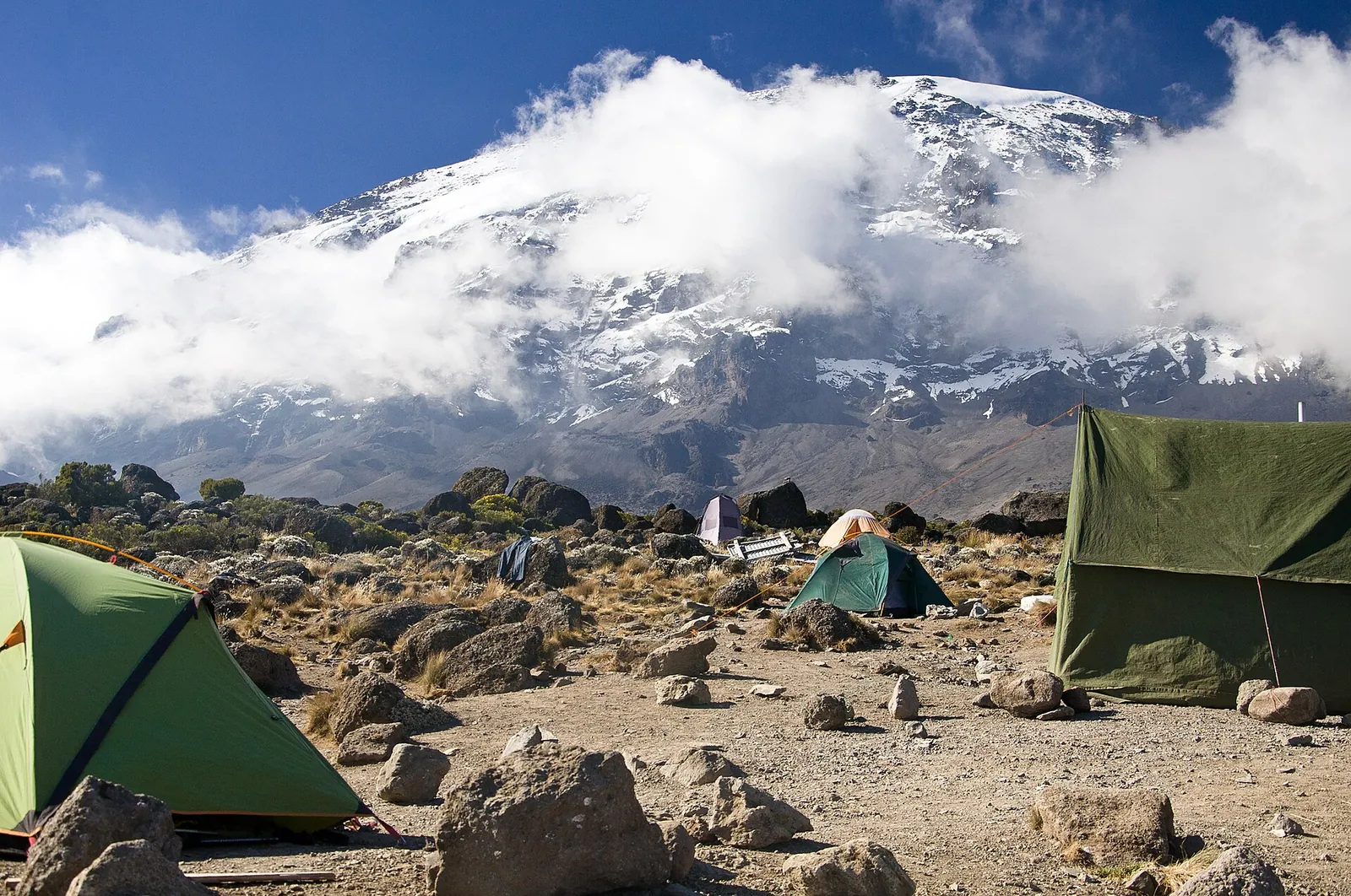 Zelte im Karanga Camp auf etwa 4.000 m im Kilimandscharo-Nationalpark, über dem Lager der wolkenumhüllte, verschneite Kibo