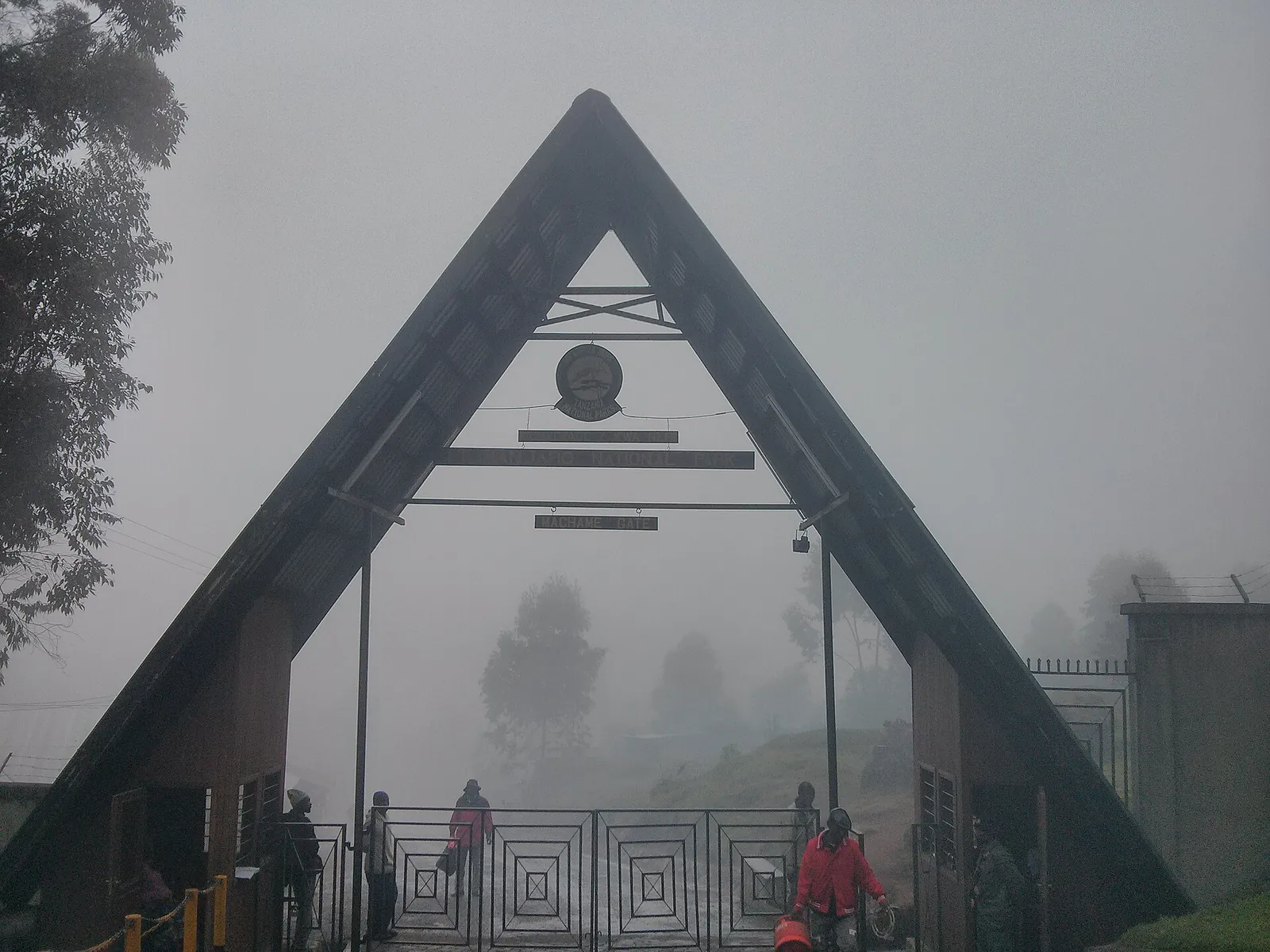 Das spitzgiebelige Tor am Machame Gate im Kilimandscharo-Nationalpark im Nebel, darunter Wanderer und Träger