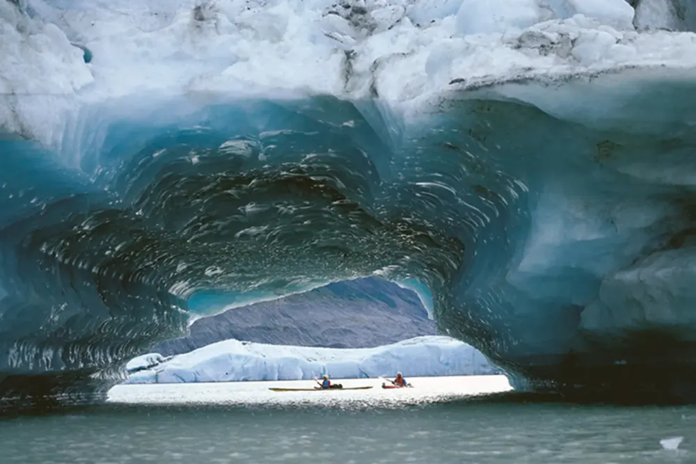 Zwei Kajaks fahren durch einen Tunnel in einem blauen Eisberg auf dem Lowell Lake am Alsek River