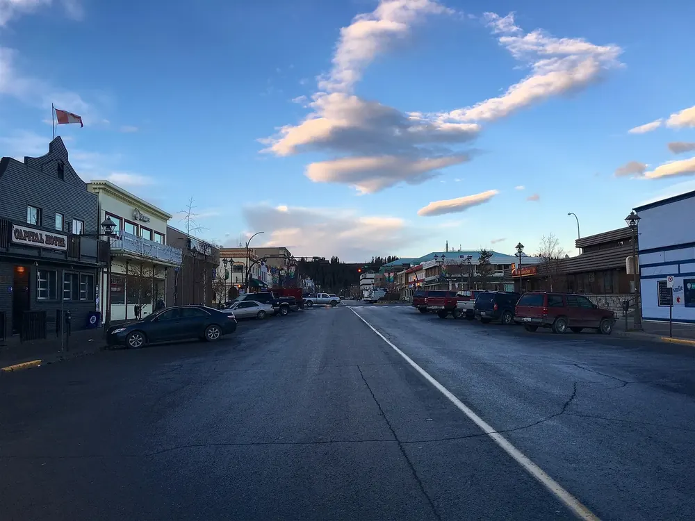 Main Street in Whitehorse in der Abendsonne: Geschäftshäuser mit Holzfassaden, parkende Autos und Quellwolken
