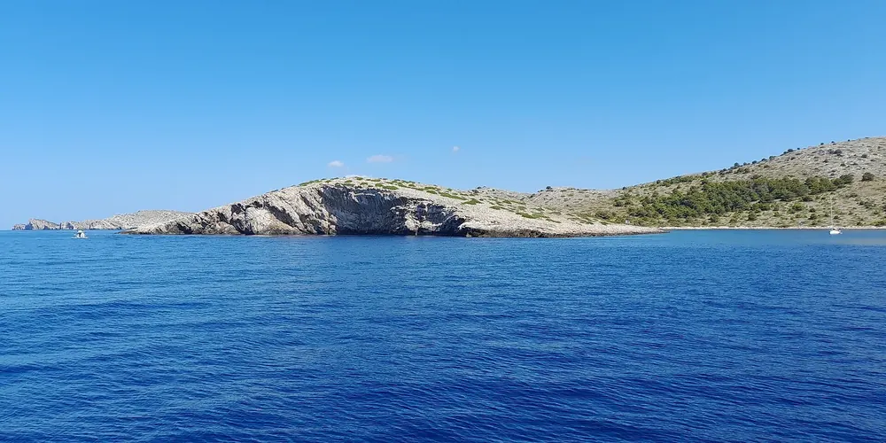 Kornaten bei Piškera: kahle, felsige Inseln mit Macchia über dem tiefblauen Meer, Piškera im Hintergrund