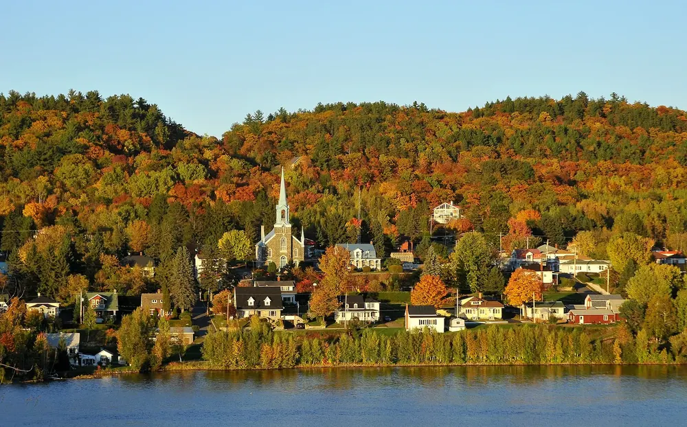 Dorf Saint-Jean-des-Piles am Saint-Maurice mit Kirchturm, umgeben von herbstlich leuchtenden Wäldern