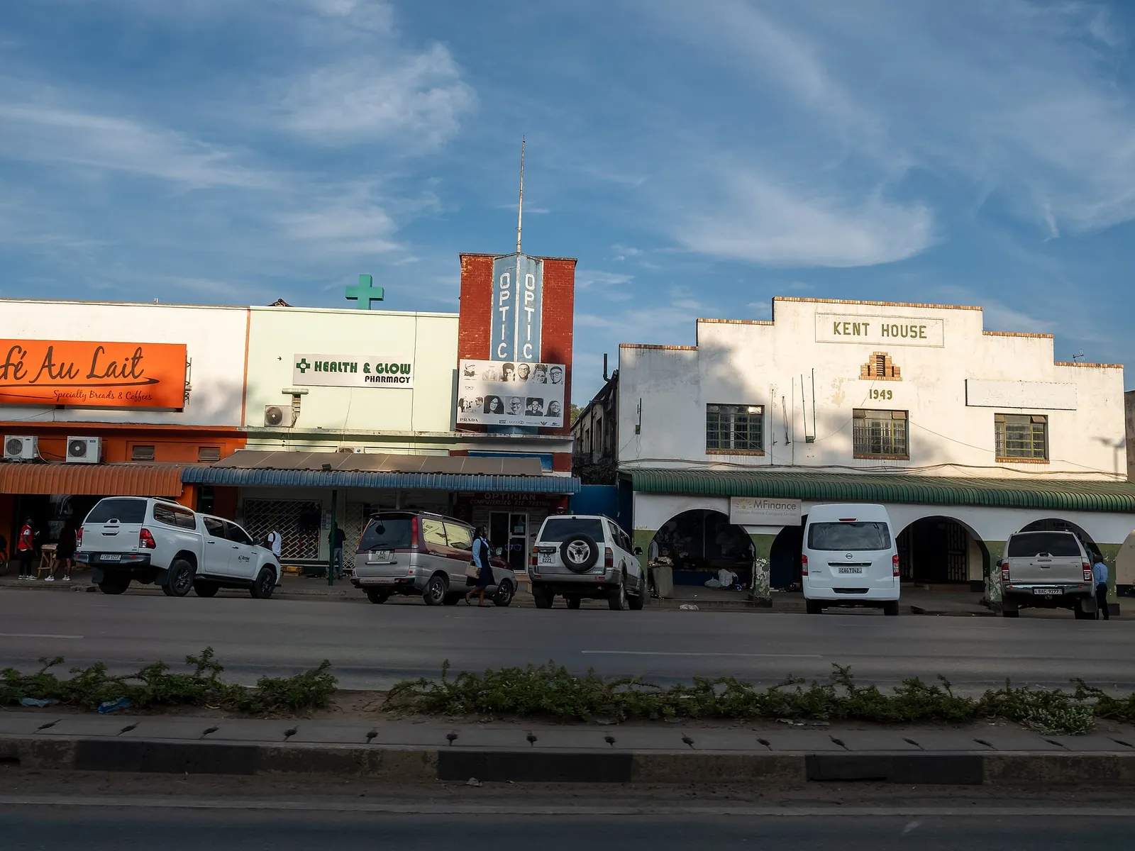 Mosi-oa-Tunya Road in Livingstone mit dem weißen Kent House von 1949 und Geschäften, davor parkende Autos