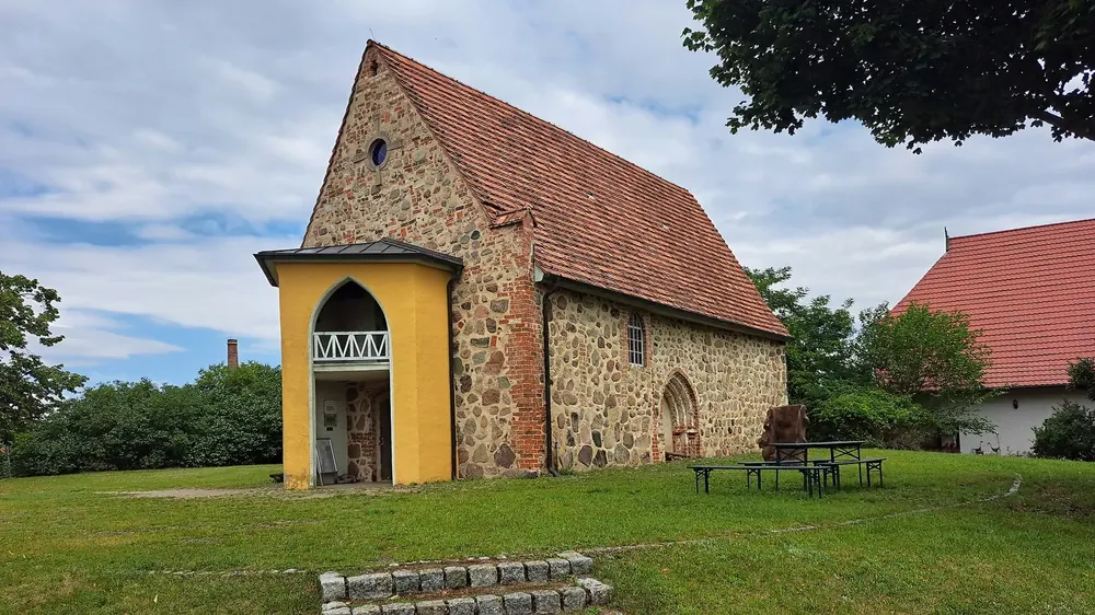 Feldsteinkirche in Federow mit gelbem Fachwerkturm und Ziegeldach auf einer Rasenfläche unter Wolken