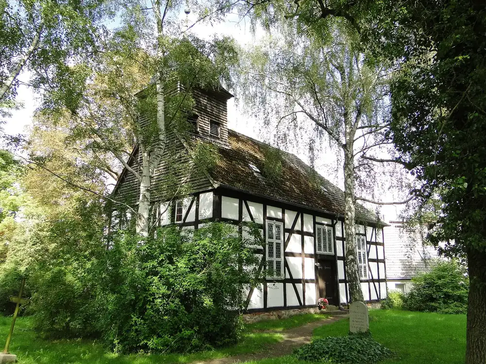 Fachwerkkirche in Kratzeburg zwischen Birken und Bäumen, mit hölzernem Dachreiter und Holzschindeln