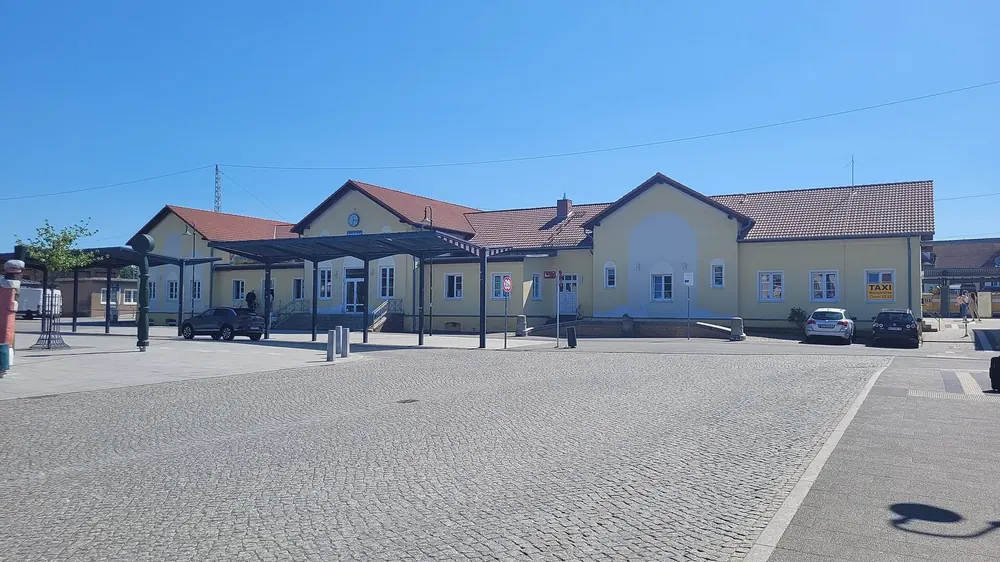 Hauptbahnhof Neustrelitz: helles Empfangsgebäude mit Bahnsteigdach hinter einem weiten gepflasterten Vorplatz